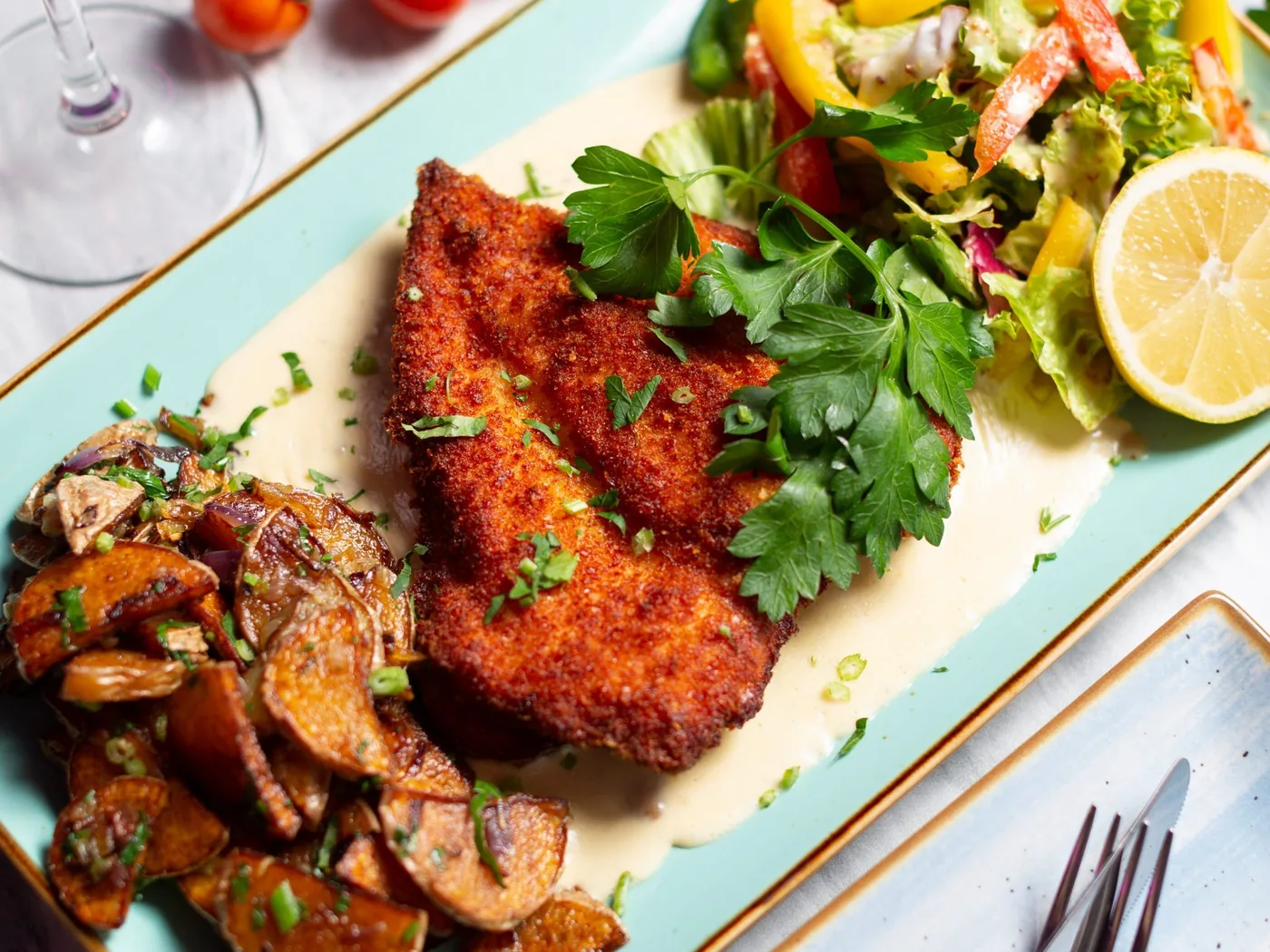Cotoletta impanata con patate saltate e insalata su un piatto turchese